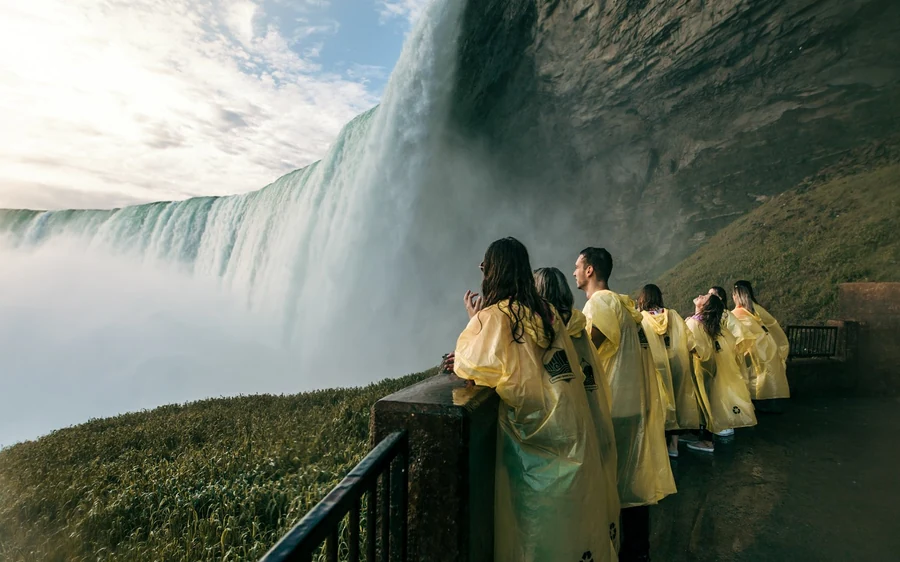 Visitors in yellow ponchos standing at a railing above the falls with mist rising
