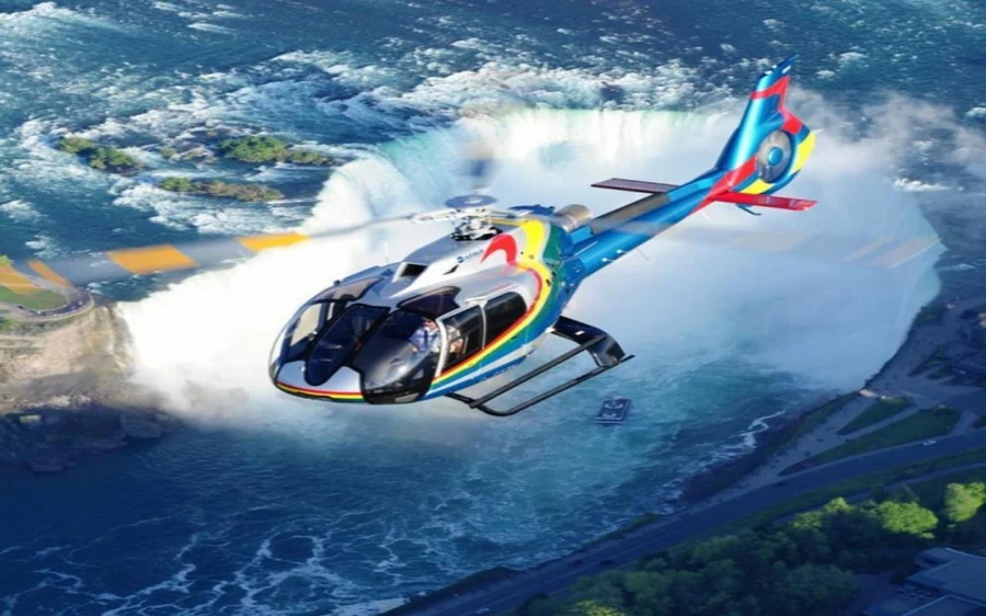 A brightly painted helicopter in flight above the white water and mist of the falls