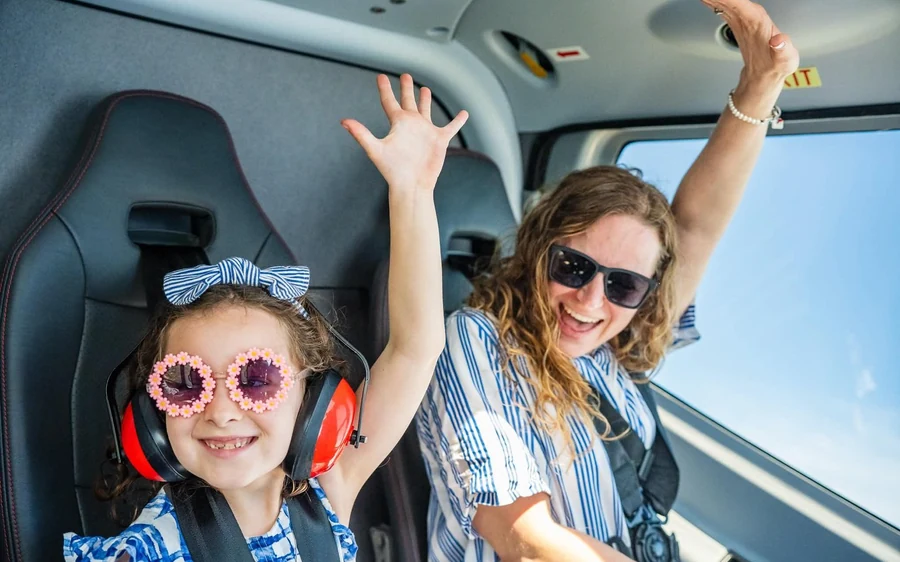 A woman and a girl in headsets inside a helicopter cabin with their hands raised