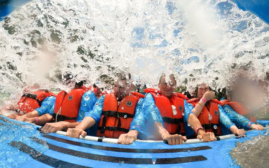 Passengers in orange lifejackets on a blue jet boat crashing through white water