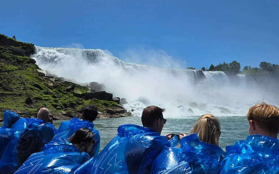 Visitors in blue ponchos at a railing looking across at the falls and the rising spray