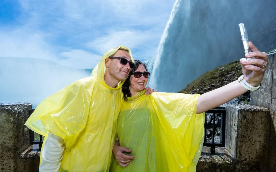 A couple in yellow ponchos taking a selfie with white falling water behind them