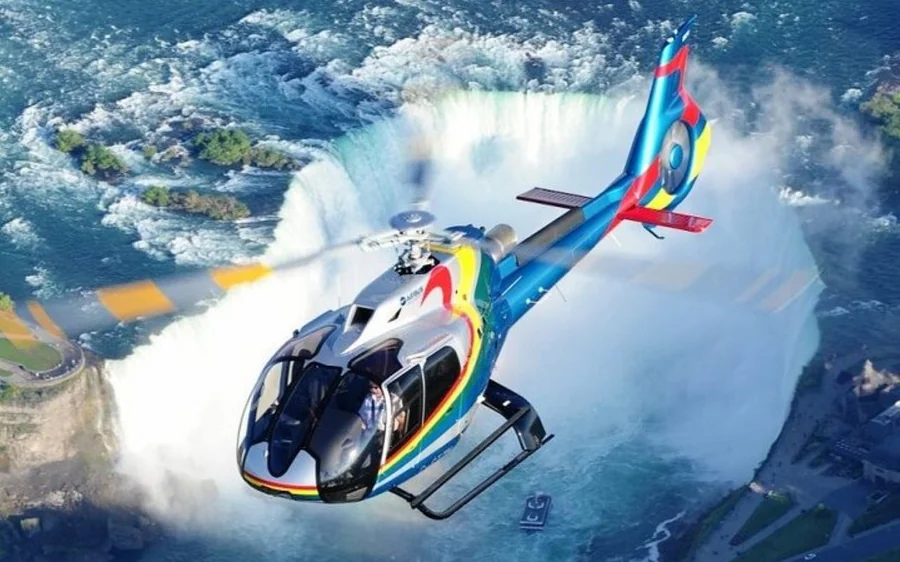 A brightly painted helicopter banking over the falls with spray rising behind it