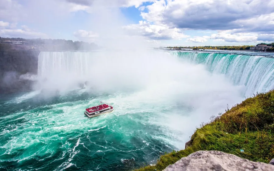An aerial view of the falls and the green river with a small orange boat below them