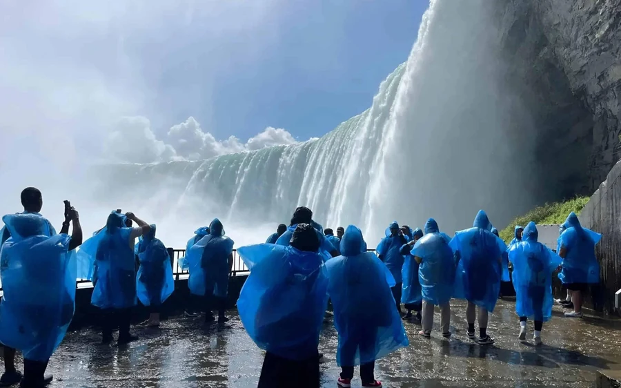 Visitors in blue ponchos walking a wet path along the gorge with the falls ahead of them